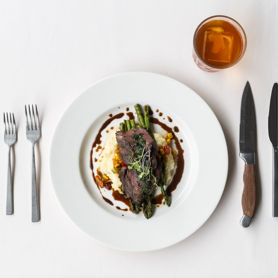 Seared steak over whipped potatoes and asparagus on a white linen place setting