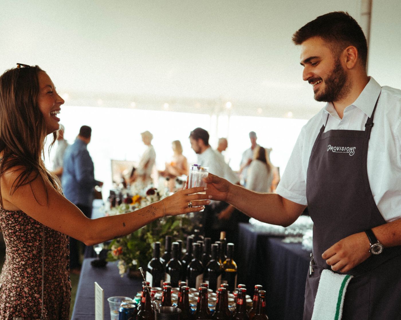 Provisions bartender handing a drink to a guest in a tent