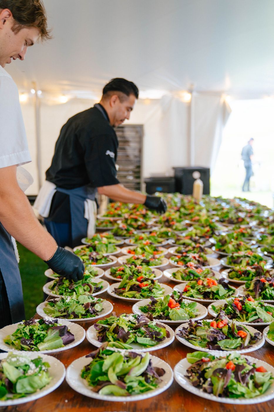 Chefs plating rows of salads under a wedding tent