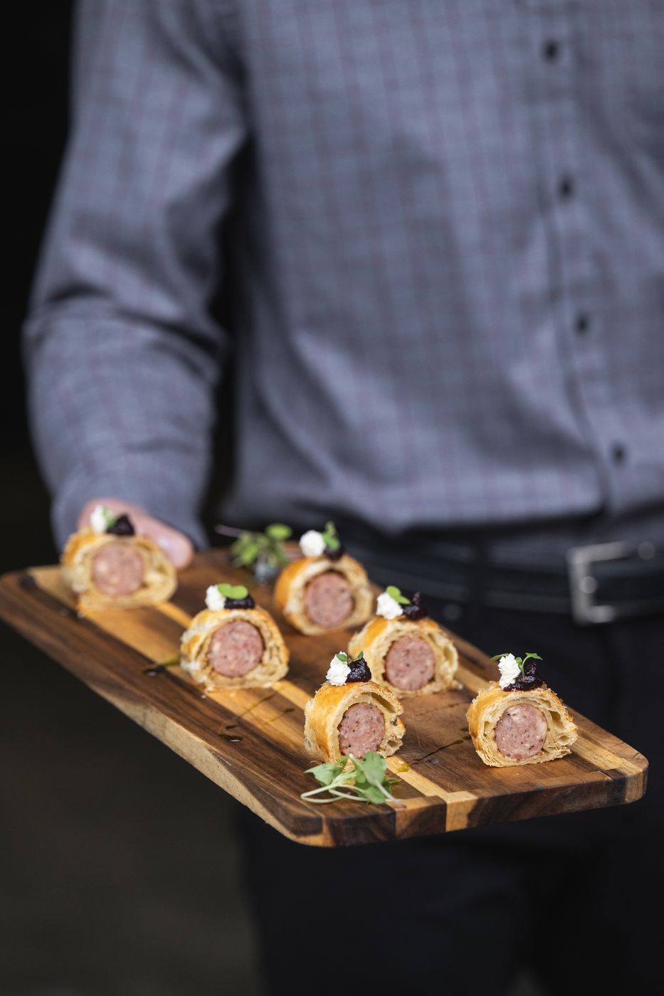 Server holding a board of mini sausage rolls