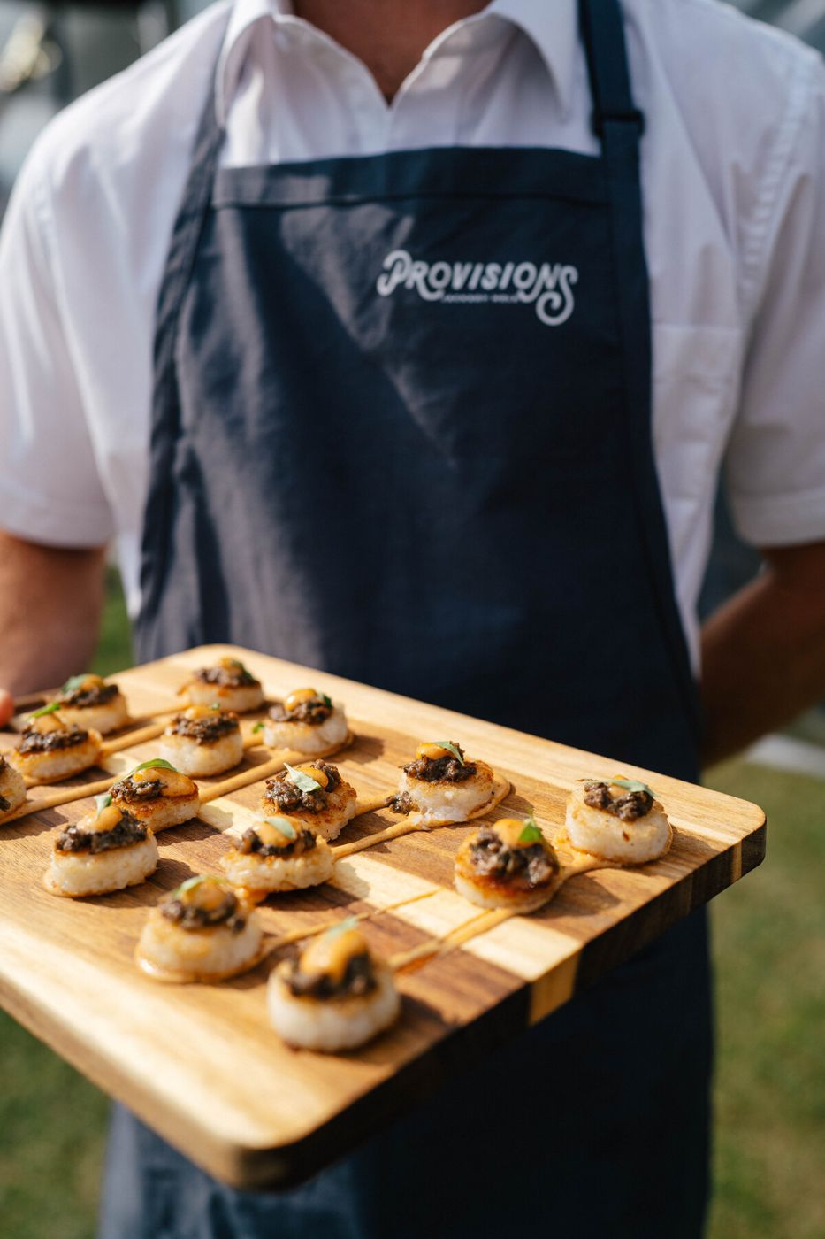 Server holding a board of mushroom bites at an outdoor event