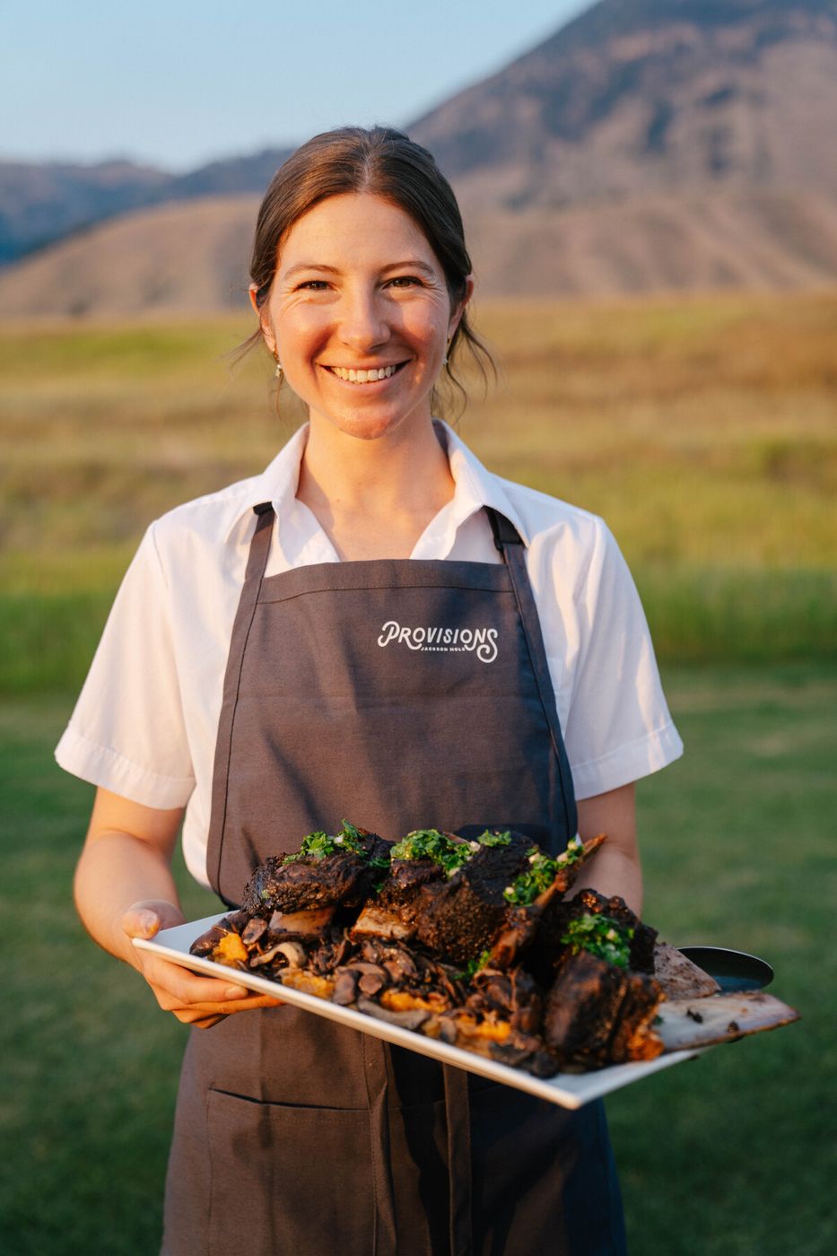 Smiling server holding a platter of short ribs with the mountains behind