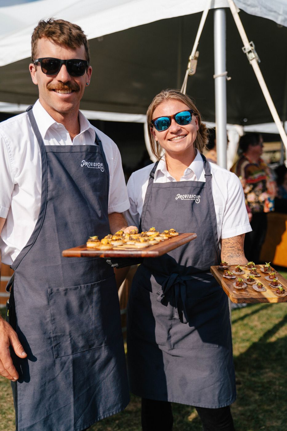 Two smiling Provisions servers holding boards of passed bites
