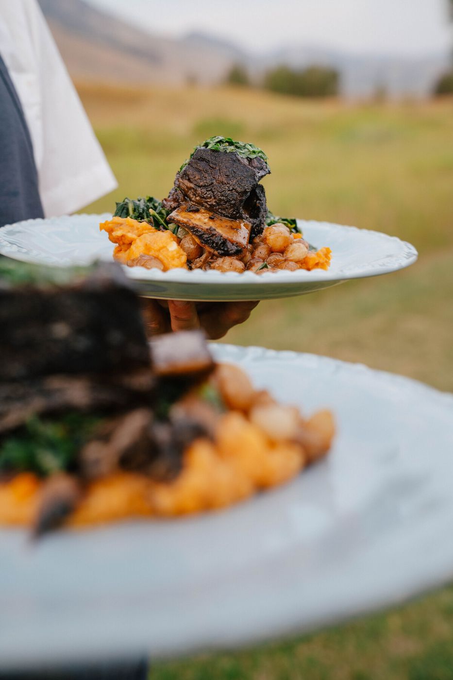 Server carrying plates of short rib outdoors