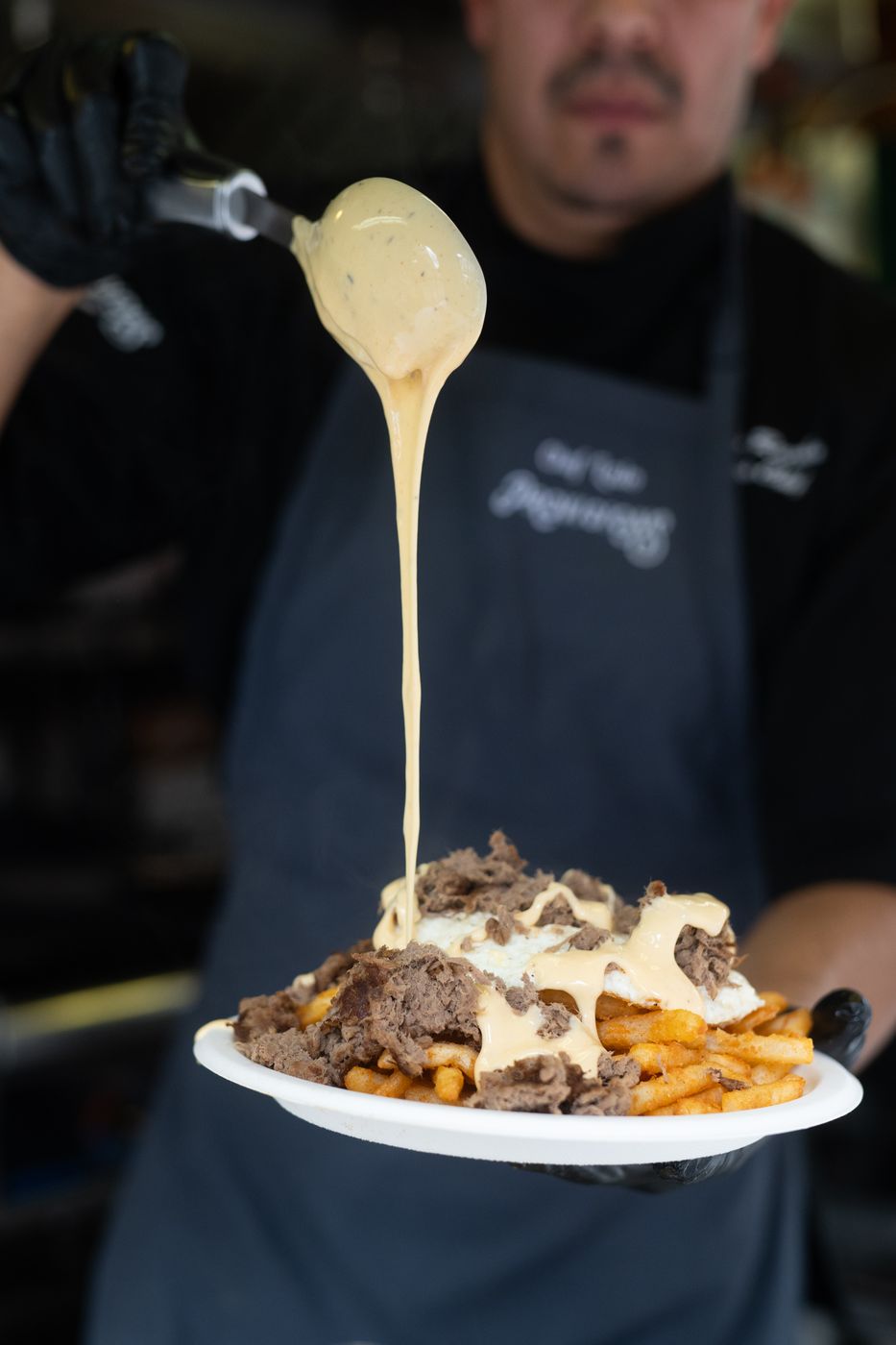 Chef pouring cheese sauce over loaded fries