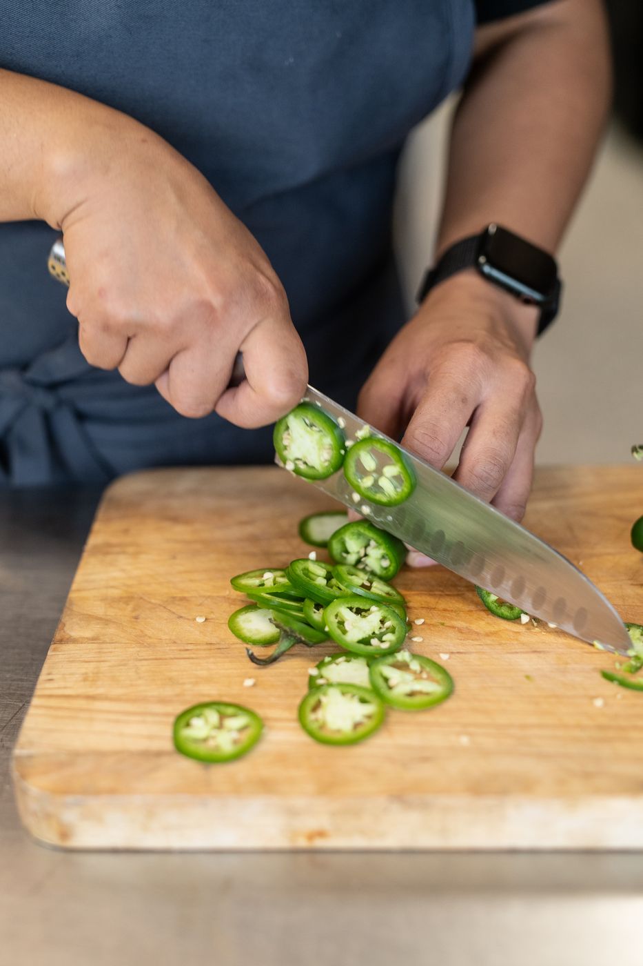 Chef slicing jalapeños on a cutting board