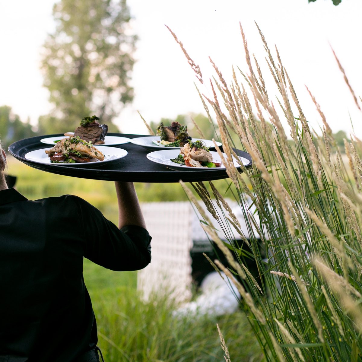 Provisions server carrying a wooden board of passed bites at an outdoor event
