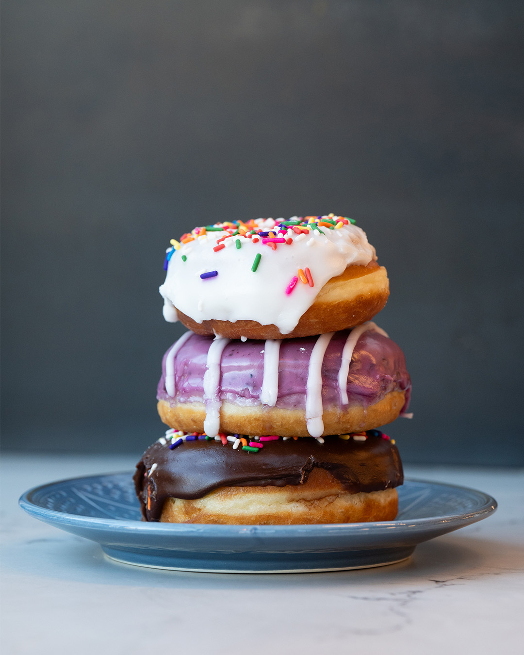 Stack of sprinkle, blueberry and chocolate donuts with a French cruller