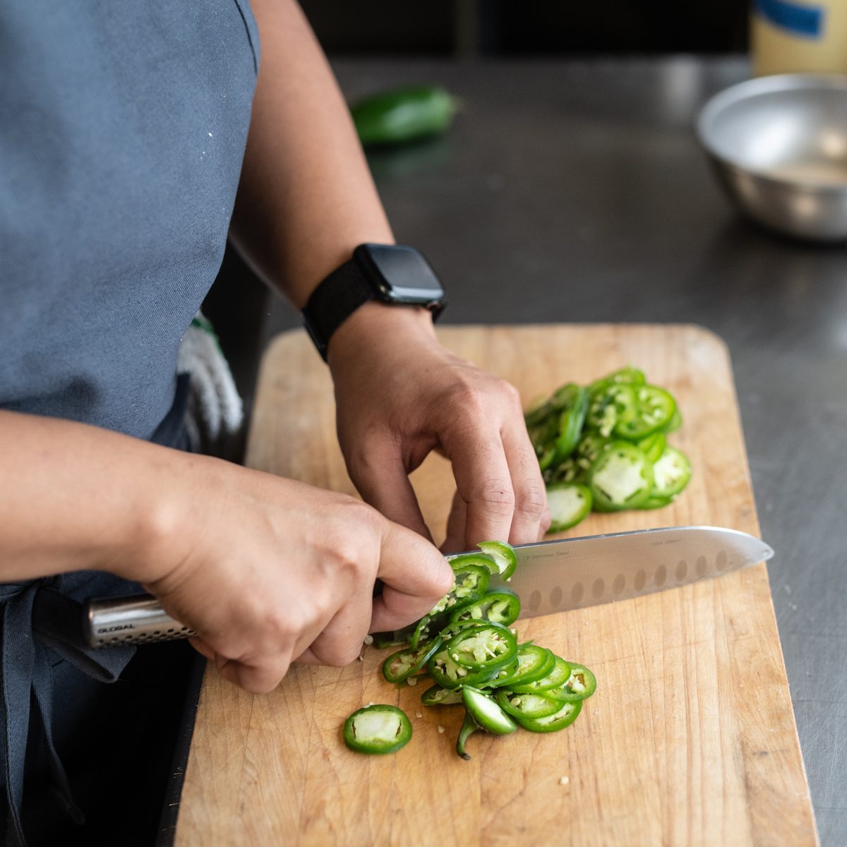 Provisions chef slicing jalapeños on a wooden cutting board