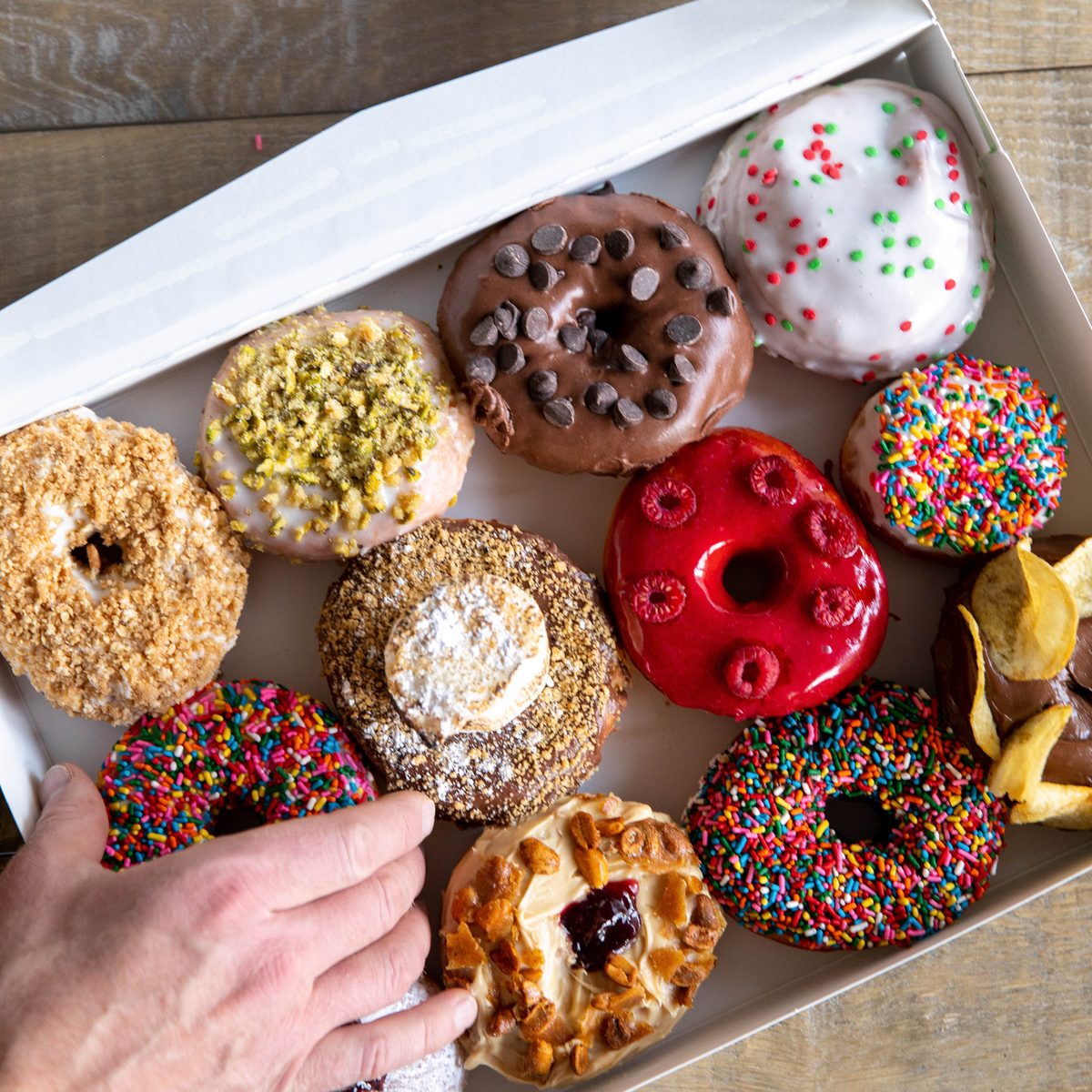 Hand reaching into a box of a dozen assorted Provisions donuts