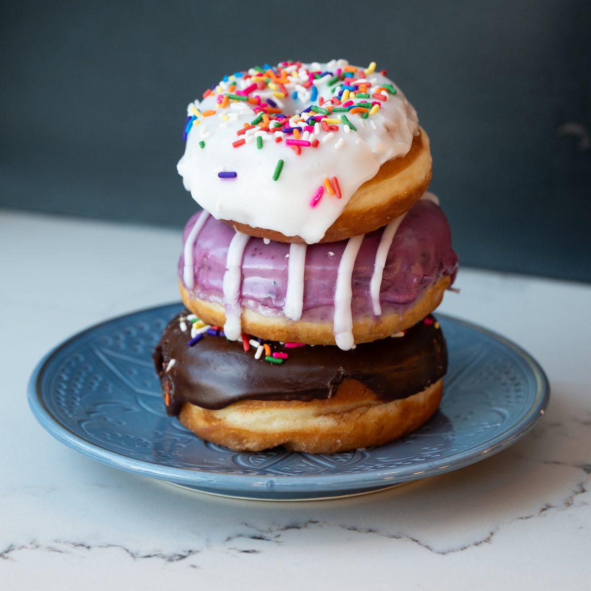 Stack of sprinkle, berry and chocolate glazed Provisions donuts on a blue plate